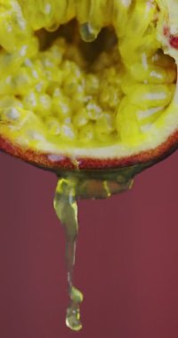 Dikey video. Pembe stüdyo arkaplanındaki doğal tutku meyvesinden akan meyve suyu fotokopi alanı ile birlikte.