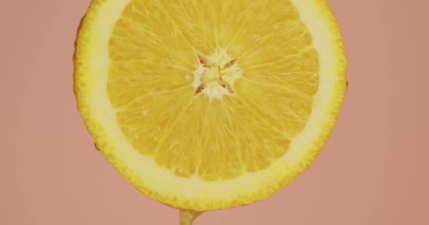 Close up of juice drops flows down on natural orange fruit on pink studio background — Stock video