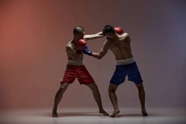 Wrestling of athletic fighting guys boxers in red light in studio, martial arts, mixed fight concept