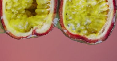 Dikey video. Meyve suyu, doğal tutku meyvelerinden, pembe stüdyo arka planında, egzotik vejetaryen yemeklerinde akıyor.