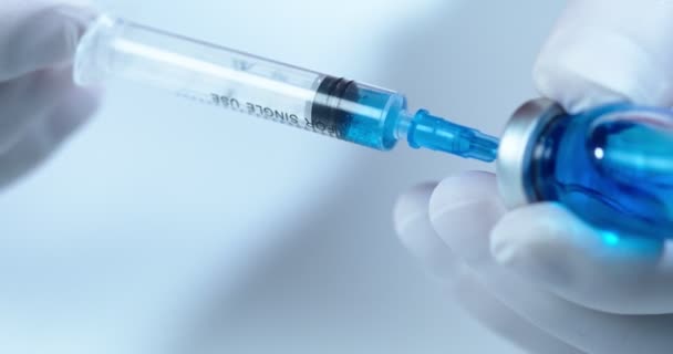 Tutup tangan dokter mengisi jarum suntik dengan vaksin biru untuk vaksinasi Covid-19 di rumah sakit. Perawatan kesehatan dan medis — Stok Video
