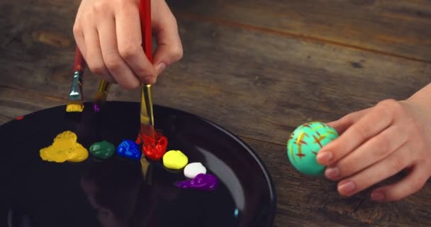 Female hands painting on Easter eggs on wooden background with palette. Natural ecological staining with food coloring — Stock Video