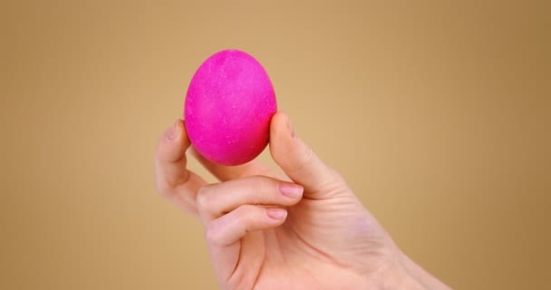 Huevo rosa de Pascua en mano femenina sobre fondo beige estudio con espacio de copia para el anuncio de vacaciones, primer plano de vídeo — Vídeo de stock