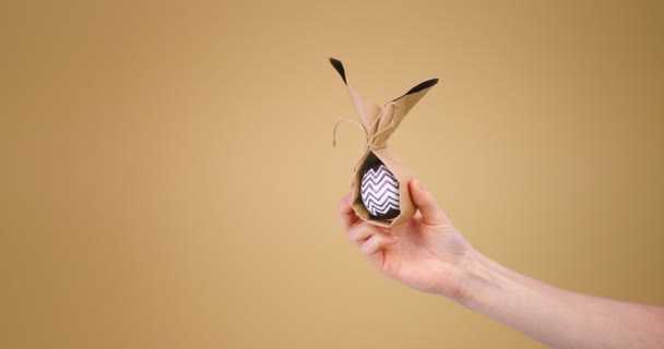 Стильное пасхальное яйцо с минималистичным шрифтом в женской руке на фоне бежевой студии с копировальным пространством — стоковое видео