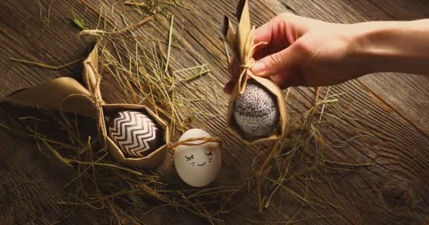 Γιορτάζουμε το Πάσχα. Γυναικείο χέρι βάζει πασχαλινό αυγό σε ξύλινο φόντο με σανό και κομψό συσκευασμένα και βαμμένα αυγά — Αρχείο Βίντεο