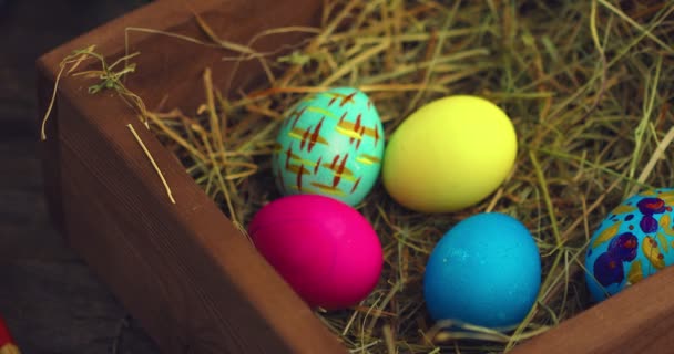 Huevos de Pascua pintados. Mano hembra poner huevo a caja de madera con heno. Primer plano de vídeo para vacaciones de primavera cristiana — Vídeo de stock