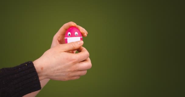 Βίντεο με γυναικεία χέρια να βγάζουν την προστατευτική μάσκα προσώπου από το αστείο πασχαλινό αυγό. Διακοπές κατά τη διάρκεια πανδημίας covid-19 — Αρχείο Βίντεο