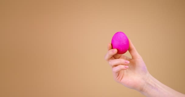 Ovo de Páscoa rosa na mão feminina no fundo do estúdio bege com espaço de cópia — Vídeo de Stock