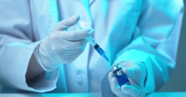 Video 'yu kapatın, doktor araştırmacıların elleri Covid-19 aşısı için cam şişeden mavi aşı dolduruyor.