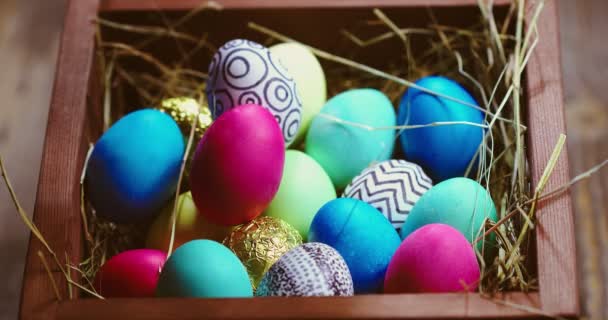 Ponga a mano el huevo de Pascua dorado en un montón de coloridos huevos pintados sobre el heno en una caja de madera, cierre el video — Vídeos de Stock