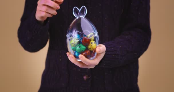 Woman opens glass vase with bunny ears full of Easter eggs. Close up video for celebrating christian religious holiday — Stock Video