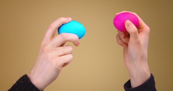 Пасхальная битва яиц. Две руки с раскрашенными красочными яйцами стучат друг друга на бежевом фоне студии, закрыть видео — стоковое видео