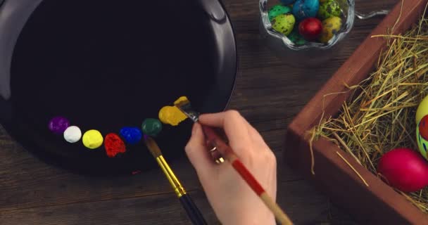 Γιορτάζουμε τις Πασχαλινές διακοπές. Χειροποίητο χέρι καλλιτέχνη με πινέλο και μπογιές στην παλέτα κατά τη διακόσμηση γιορτινών αυγών — Αρχείο Βίντεο