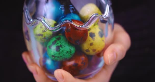 Vrouwelijke hand met glazen vaas vol met beschilderde kleurrijke kwarteleitjes. close-up video voor het vieren van christelijke vakantie — Stockvideo