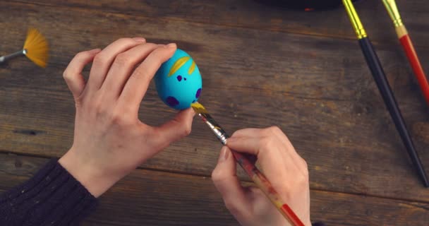 Easter egg in female artists hands. Close up top view video of woman painting patterns on eggshell with paintbrush — Stock Video