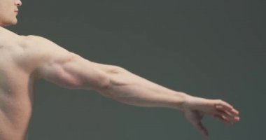 Kaslı erkek eli. Atletik adam gri stüdyo arka planında fotokopi alanı olan pazılarını gösteriyor. 4K videosunu kapat.
