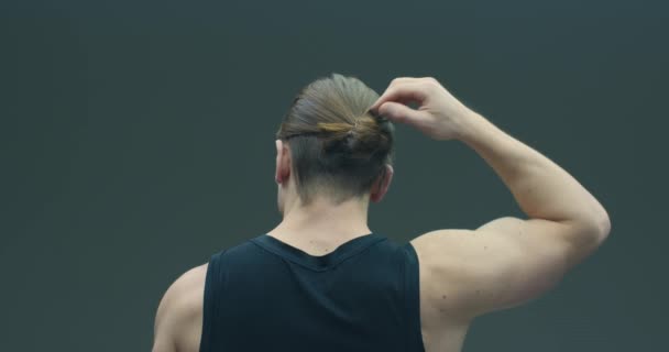 Vídeo de un tío de pelo largo bajándose el pelo sobre un fondo gris de estudio. Vista trasera. Concepto de cuidado del cabello. Anuncio de champú — Vídeo de stock