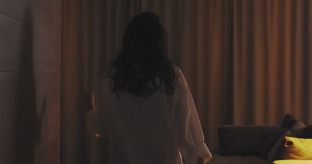 4k wideo młodej kobiety z długimi włosami otwierające zasłony patrząc ciesząc się światłem w przytulnym wnętrzu apartamentu lub hotelu — Wideo stockowe