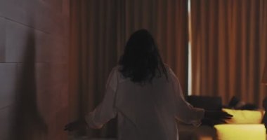 4K video, perdeleri açan genç bir kadının görüntüsü. Sabahın köründe rahat bir dairede ya da otelde keyif çatıyor.