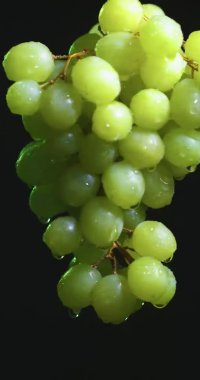 Dikey video. Üzüm kaplı üzüm bağları siyah stüdyo arkaplanı, meyve vitaminleri, sağlıklı beslenme konsepti üzerinde dönüyor