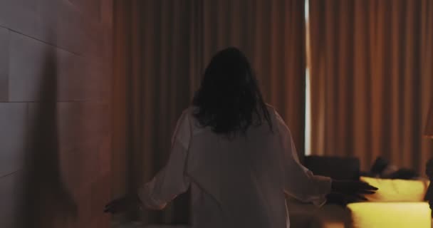 4k видео, вид сзади на молодую женщину, открывающую шторы и наслаждающуюся светом утром в уютной квартире или отеле — стоковое видео