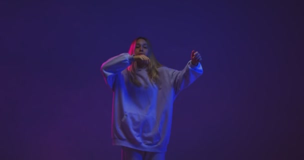 4k video van een stijlvol jong meisje, cool dansen in een hoodie in neon licht en achtergrond. — Stockvideo