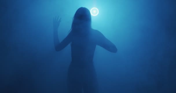 Silhouette of dancing young girl in neon blue light and smoke. Modern dance in haze at night party — Vídeo de stock