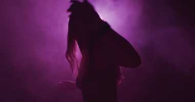 Renkli neon ışıklı ve gece dumanlı dans eden genç kız silueti. Puslu modern dansın 4k videosu