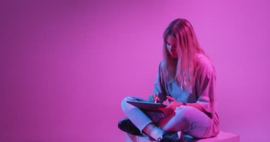 Tablet bilgisayarı olan modern bir kız. Genç blog tasarımcısı çizer. Renkli Neon ışığı ve arkaplan