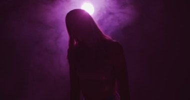 Violet Neon ışıklı ve puslu dans eden genç kız. Kadın silueti ve gece dumanının 4k videosu. Modern dans