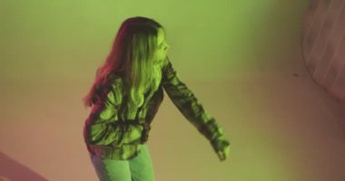 Renkli stüdyo ışığında dans eden uzun saçlı şık bir genç. Modern dansın 4k videosu
