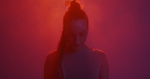 Silhouet van jong gemengd ras meisje met paardenstaart kijken naar camera in rood licht in studio met rook — Stockvideo