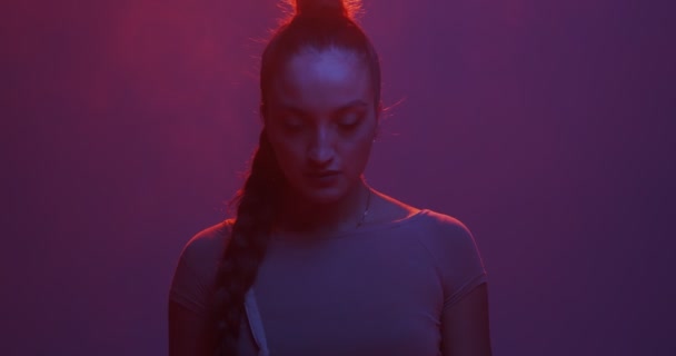 Stijlvol jong gemengd ras meisje in neon licht in de studio met rook kijken naar camera, headshot — Stockvideo