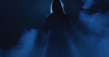 Gizemli gece sisi ve neon mavi ışıkta kadın silueti. 4k kadın ve sigara videosu