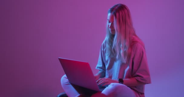 4k段现代年轻女性博主带着手提电脑打字的视频。彩色霓虹灯和背景 — 图库视频影像
