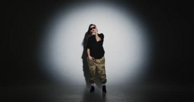 Stüdyoda güneş gözlüklü genç kız sahne ışıkları altında dans ediyor. Modern kadın dansçı serbest dans gösterisi yapıyor..