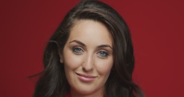 Mooi jong georgiaans meisje brunette met gezonde lange haren, perfecte make-up glimlachen op rode studio achtergrond — Stockvideo