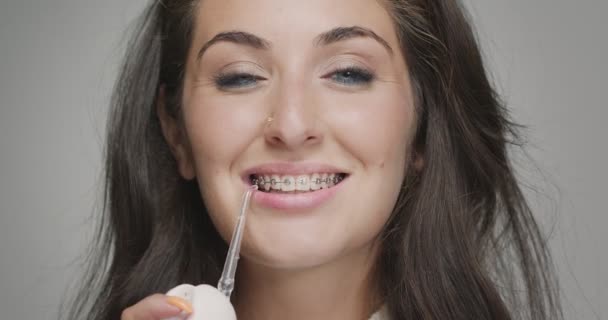 Vízfogselyem, fogászati öntözőkészülék fogszabályzáshoz. Csinos lány tisztítja a száját a tábláról. Higiéniai rutin, fogászat — Stock videók
