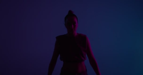 Молодая расовая девушка танцует в неоновом студийном свете. Профессиональная исполнительница, поднимающая руки — стоковое видео