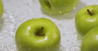 Yeşil elmalar su üzerinde yuvarlanırken birbirleriyle çarpışıyor, beyaz zeminde doğal meyveler, sağlıklı yiyecekler.