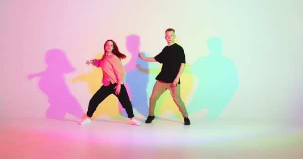 Cool jeune couple dansant se déplaçant synchrone dans la lumière colorée du studio. Danse contemporaine, danseurs hip hop — Video