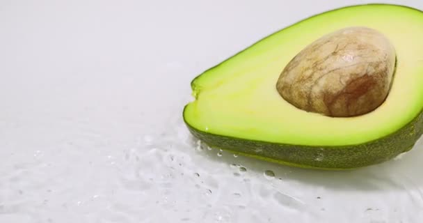 Mitad aguacate verde maduro, acostado en agua corriente. Fruta orgánica natural sobre fondo blanco. Vitaminas, alimentación saludable — Vídeos de Stock