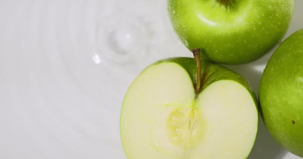 Pommes vertes couchées dans l'eau, gouttes tombantes, éclaboussures. Fruits naturels sur fond blanc, alimentation saine — Video