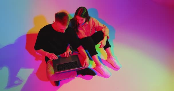 Modern lány és srác laptoppal, programozók, akik számítógépen dolgoznak, projektet készítenek. Színes neon fény és háttér. — Stock videók