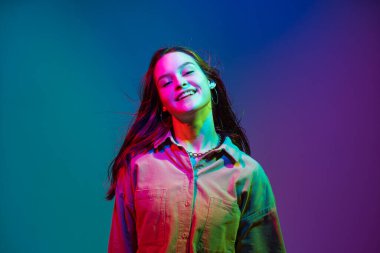 Gülümseyen, uzun, sağlıklı saçları olan, renkli neon renkli stüdyo ışıklarıyla gülen modern bir genç kız. Yaratıcı güzellik portresi