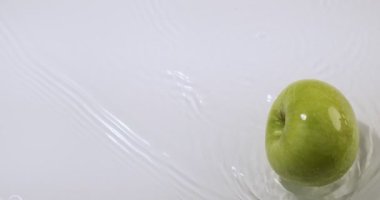 Suda yeşil elmalar yuvarlanıyor, beyaz stüdyo arka planında doğal eko meyveler, vitaminler ve sağlıklı beslenme konsepti