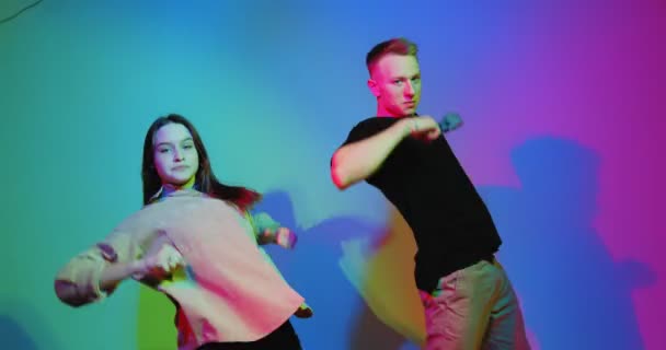 Bailando pareja joven fresco moviéndose en la luz colorida estudio de neón. Escuela de danza contemporánea, bailarines de hip hop — Vídeos de Stock