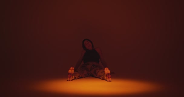 Positieve jonge meisje danser wachten of neem een pauze, zitten slingerende voeten op de dansvloer in de schijnwerpers in de studio — Stockvideo