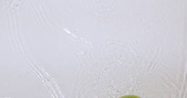 Suda yeşil elmalar yuvarlanıyor, beyaz stüdyo arka planında doğal meyveler, vitaminler ve sağlıklı beslenme konsepti.