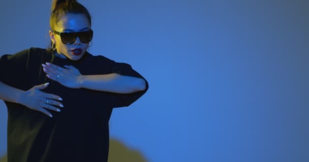 Menina rapper elegante dançando a música executando freestyle hip hop dança em néon luz estúdio azul. Espaço de cópia para anúncio — Vídeo de Stock